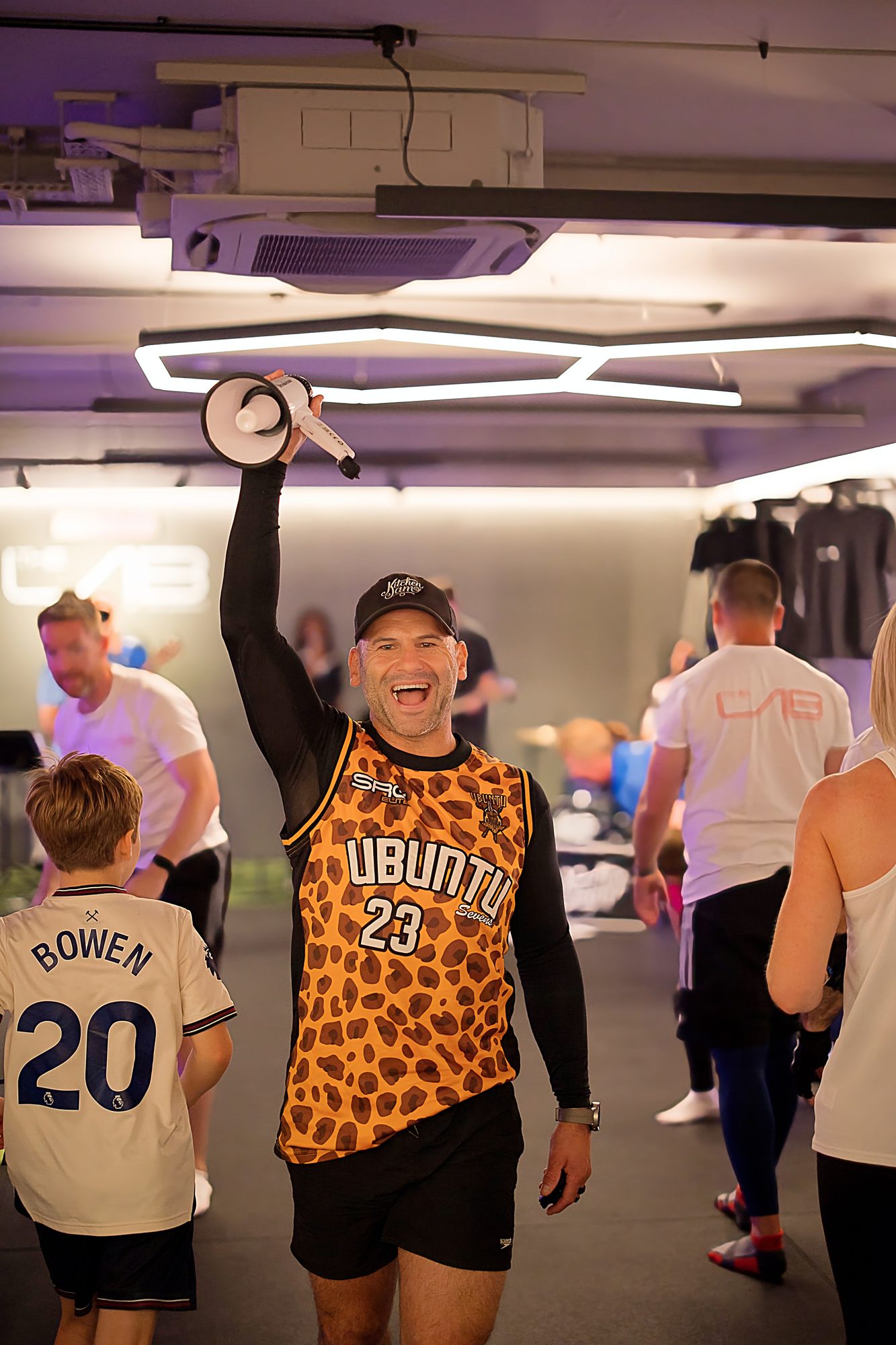 Barry de Jager grinning and raising a megaphone at a lively community fitness event