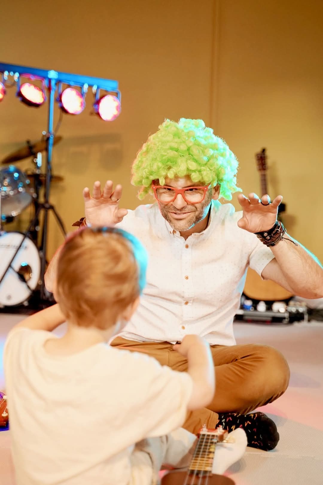 Barry de Jager performing on the floor, hands raised, facing a small child during a Baby Concert