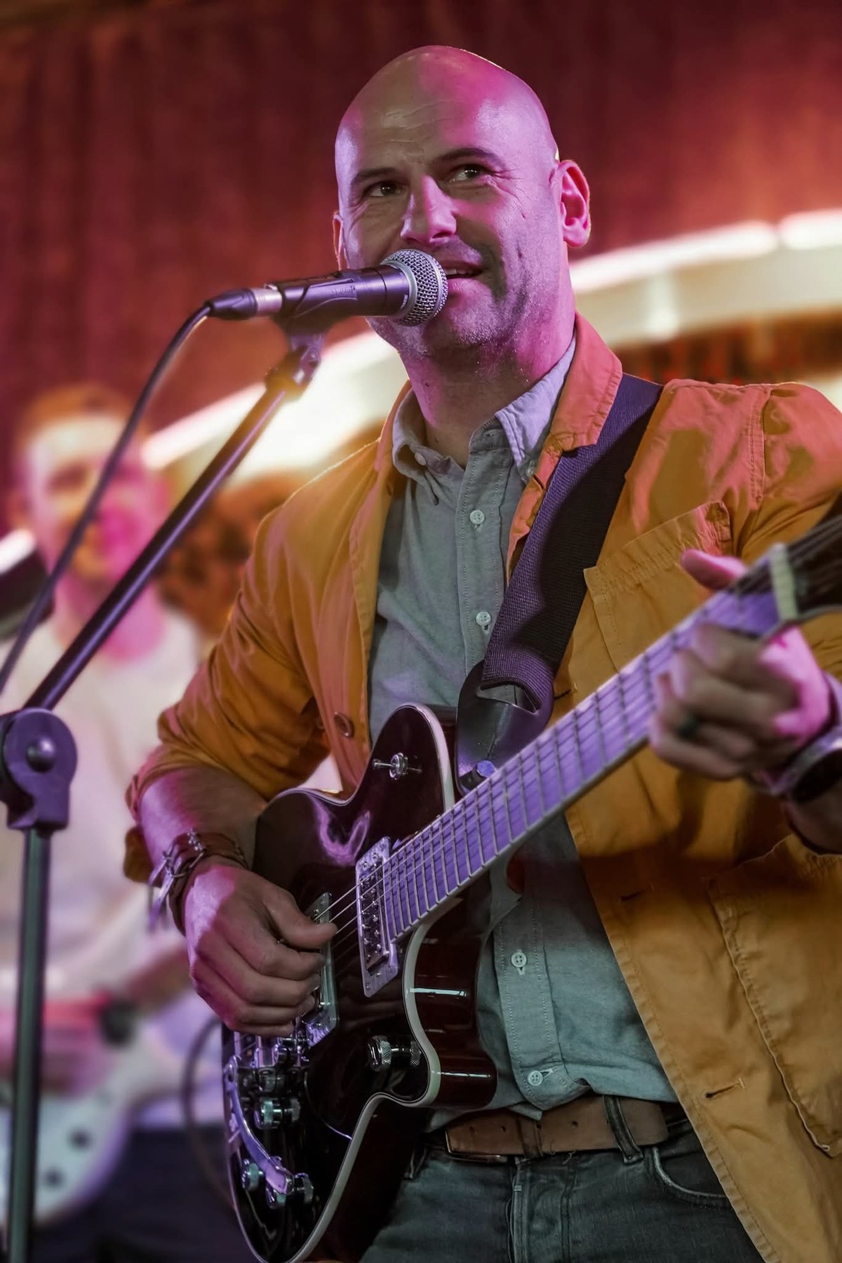 Barry de Jager singing into the microphone with an electric guitar under warm stage lighting