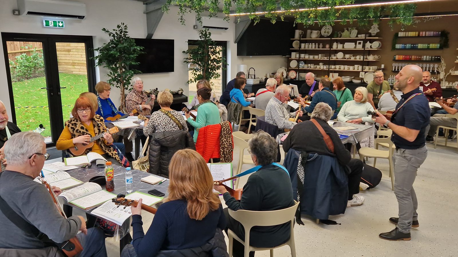 Barry de Jager leading a room full of ukulele players seated around tables