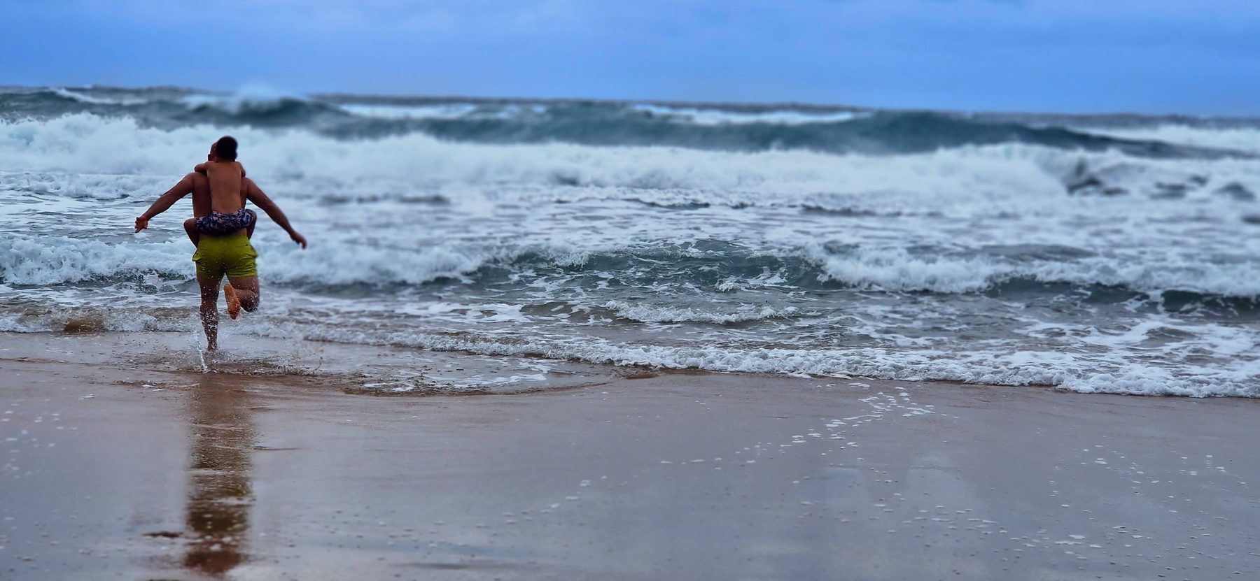Barry de Jager walking into a rough, wind-driven sea under a grey sky